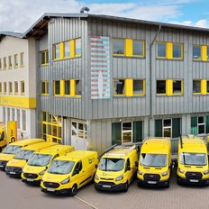 Ein modernes Gebäude mit gelben Fenstern und einer bunten Wandgestaltung, umgeben von mehreren gelben Lieferwagen.