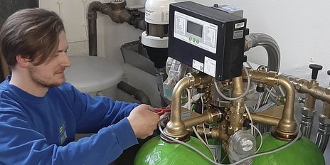 Der Techniker in blauer Kleidung verwendet Zangen, um an einer grünen Druckbehälteranlage mit goldenen Armaturen zu arbeiten.