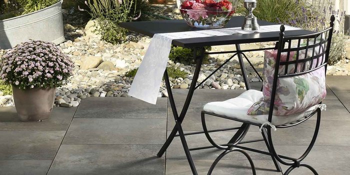 Ein eleganter Tisch mit einer weißen Tischdecke steht im Freien, umgeben von bunten Blumen und Steinen.