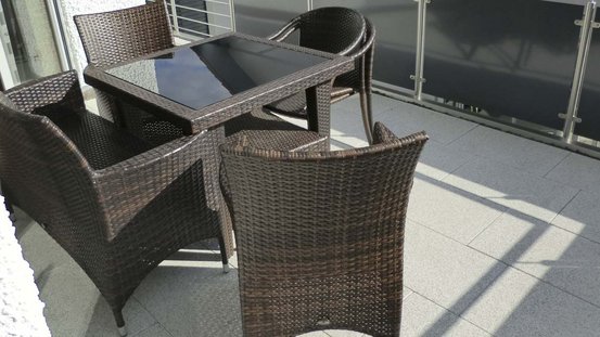 Ein eleganter Balkon mit einem Tisch und vier Stühlen aus geflochtenem Material, ideal für entspannte Stunden im Freien.