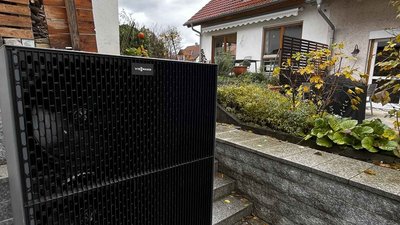 Das Heizgerät mit einem Gitterdesign steht vor einem gepflegten Garten, während die Wolken den Himmel bedecken.