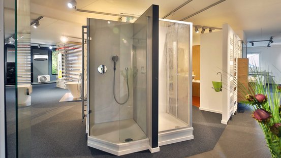 Der Ausstellungsraum zeigt elegante Duschlösungen, umgeben von modernen Badezimmermöbeln und einer grünen Pflanze im Vordergrund.