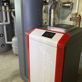 Ein moderner Heizkessel steht in einem Kellerraum, umgeben von Rohren und einem großen Wassertank im Hintergrund.