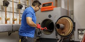 Ein Techniker in blauer Uniform reinigt eine Heizungsanlage mit einem Werkzeug in der Hand, während er konzentriert arbeitet.