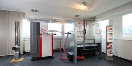 Der Heizkessel ist mit roten Schläuchen verbunden und zeigt eine technische Übersicht an der Wand neben ihm.