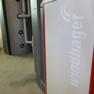 Ein modernes Heizsystem mit einer auffälligen weißen Front und dem Logo 'windhager' ist im Vordergrund zu sehen.