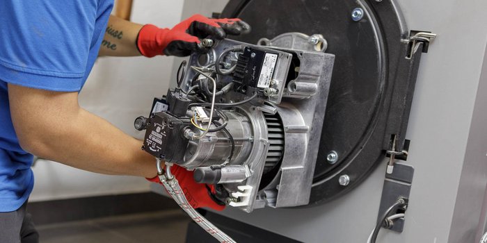 Eine Person in blauer Kleidung und roten Handschuhen arbeitet an einem Motor, während sie Kabel und Teile hält.