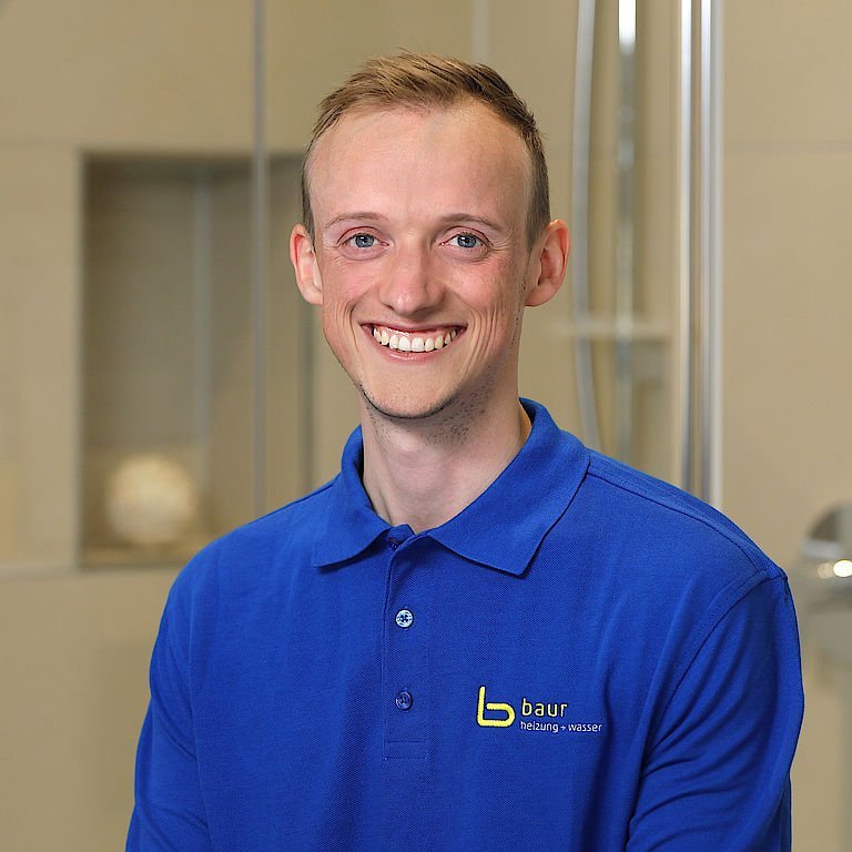 Der Mann in einem blauen Shirt strahlt Freude aus, während er in einem hellen, eleganten Badezimmer posiert.