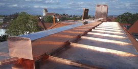 Ein Kupferdach mit schimmernden Platten bietet einen Blick auf die Stadt, während Wolken am Himmel vorbeiziehen.