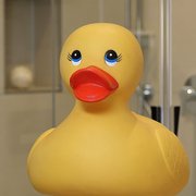 Fröhliche Gummiente in einem modernen Badezimmer Eine große gelbe Gummiente mit roten Lippen und großen Augen steht vor einem hellen Hintergrund, der eine entspannende Atmosphäre schafft.