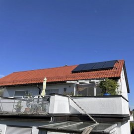 Ein modernes Haus mit einem roten Ziegeldach und Solarpanelen, unter einem strahlend blauen Himmel.