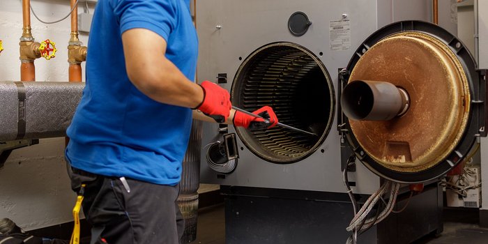 In einem Heizungsraum wird ein Ventilator von einem Techniker mit einem langen Werkzeug gründlich gereinigt.