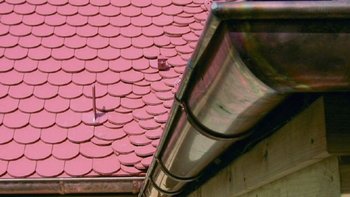 Die Aufnahme zeigt ein traditionelles Schindeldach in leuchtendem Rot, ergänzt durch eine metallische Regenrinne an der Seite.