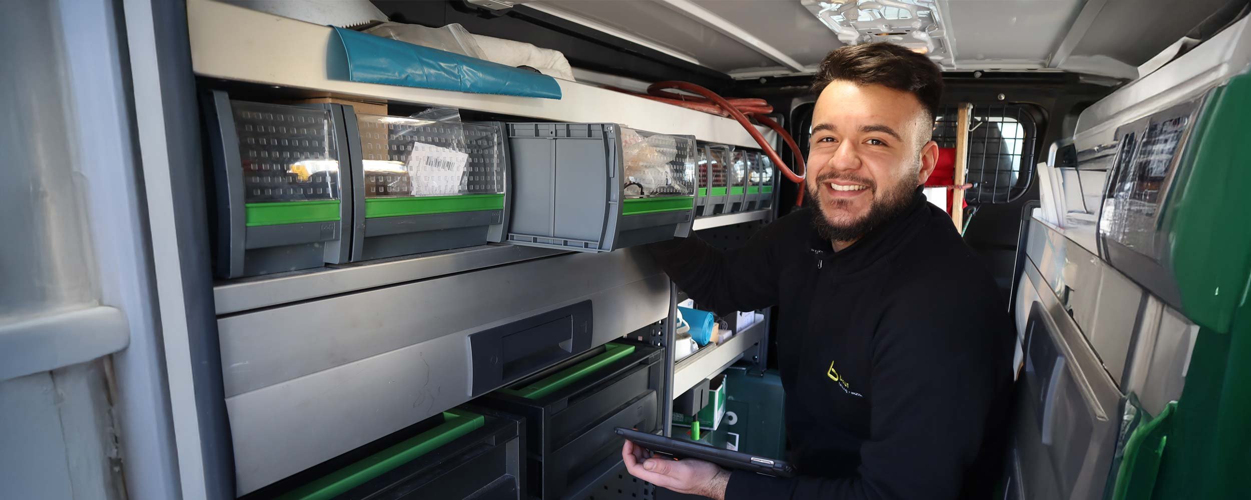 Der Mann im Lieferwagen hat ein Tablet in der Hand und lächelt, während er seine Arbeitsutensilien organisiert.