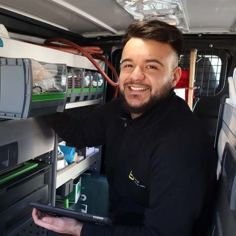 Der Mann im Lieferwagen hat ein Tablet in der Hand und lächelt, während er seine Arbeitsutensilien organisiert.