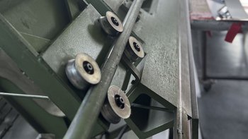 Nahaufnahme einer Produktionsmaschine mit grüner Lackierung Eine Nahaufnahme von Maschinenrollen, die auf einer grünen Metalloberfläche montiert sind, mit einem unscharfen Hintergrund.