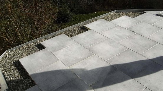Eine moderne Terrasse mit großen, grauen Fliesen, die in einem ansprechenden Muster verlegt sind, umgeben von Kies.