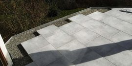 Eine moderne Terrasse mit großen, grauen Fliesen, die in einem ansprechenden Muster verlegt sind, umgeben von Kies.